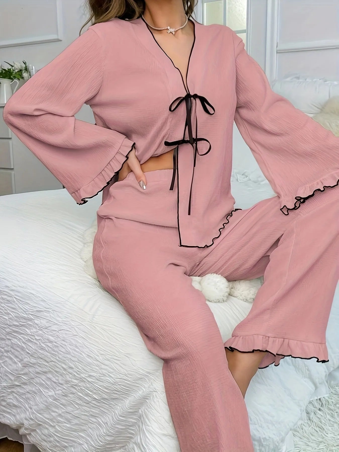 Pink pajama set with black trim worn by a person on a white bed.